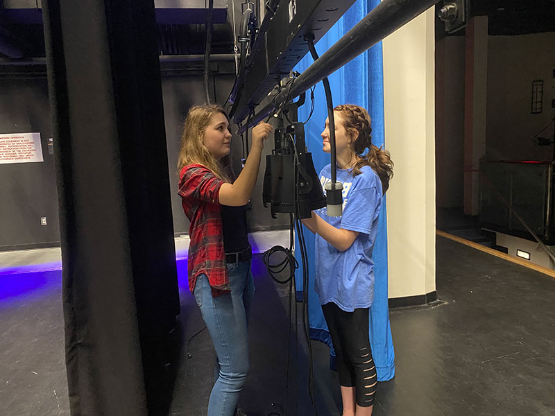 Junior Angelina Jonkaitis and sophomore Brooke Holland finish up moving a light. The lights were arranged five to a line in order to get the zones correct on the lightboard.
