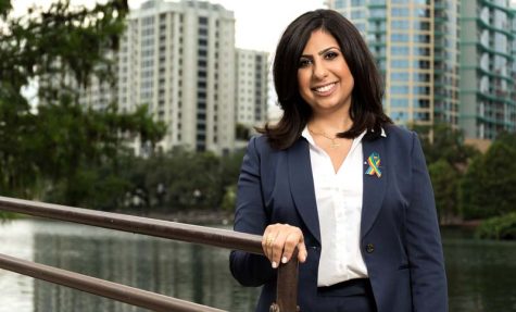 Orlando politician Anna Eskamani poses by Lake Eola, surrounded by high-rise buildings.