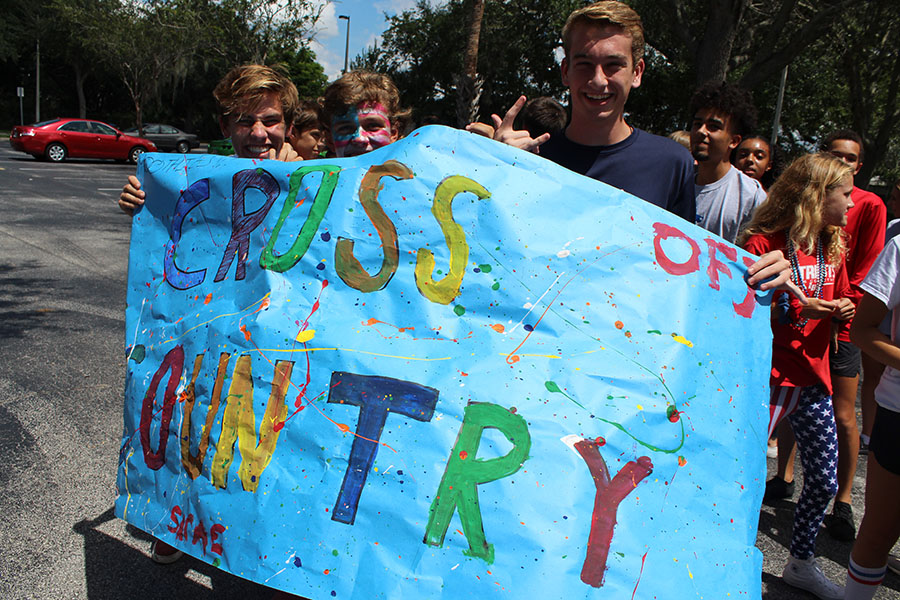 Cross Country runners junior Gavin Koerth, sophomore Carson Yore, and Junior Zion Van der sanden hold up their team sign minutes before walking in the homecoming parade. The Cross Country team gathered together and walked in their freedom friday attire.
