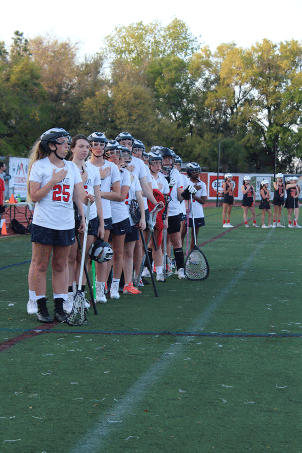 The junior varsity teams stand for the national anthem before their game begins on Monday, March 4 . The junior varsity and varsity girls lacrosse teams played against Winter Park High School in Darwin Boothe Stadium with the junior varsity team winning at 10-4 and the varsity team losing at 8-10.