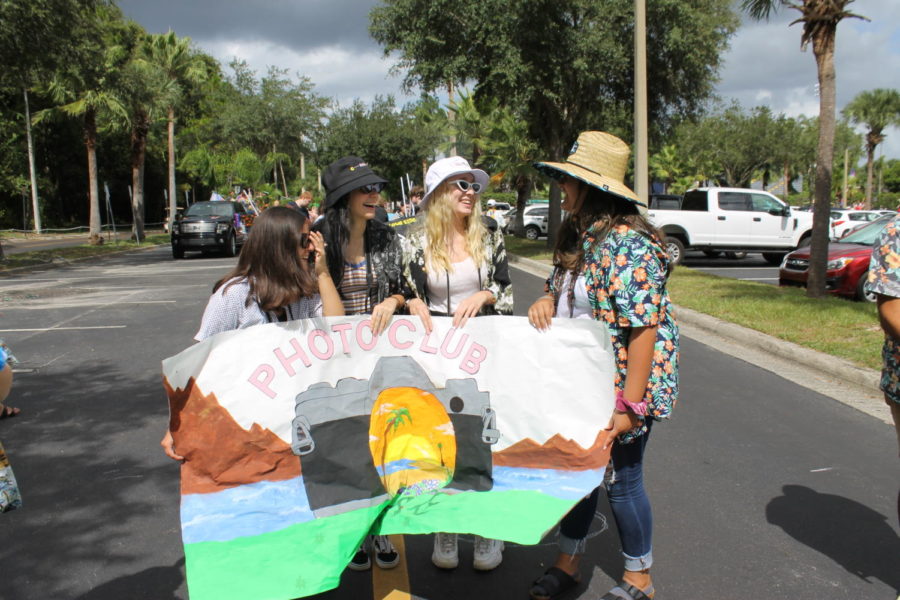 Freshmen Samantha Peraza Salek, Uliana Ermolaeva, Annie Kucera and Mya Loor smile with their poster for photography club on Thursday, October 10 at the homecoming parade. Clubs decorated their signs with beach-themed decor to fit the homecoming theme of Escape to Paradise.