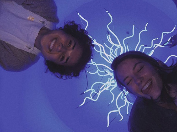 Seniors Anna Cinq-Mars and Andrea Romero smile using a light exhibit as their backdrop at the Dale Chihuly Museum studio in St. Petersburg, FL on Nov 19. Many modern artists have begun using techniques that allow the viewer to become a part of the art.